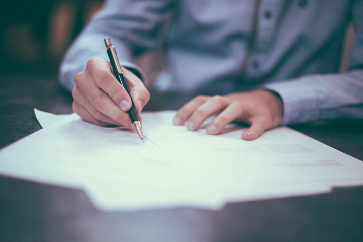 Legal documents and a pen on a desk, family members in the background